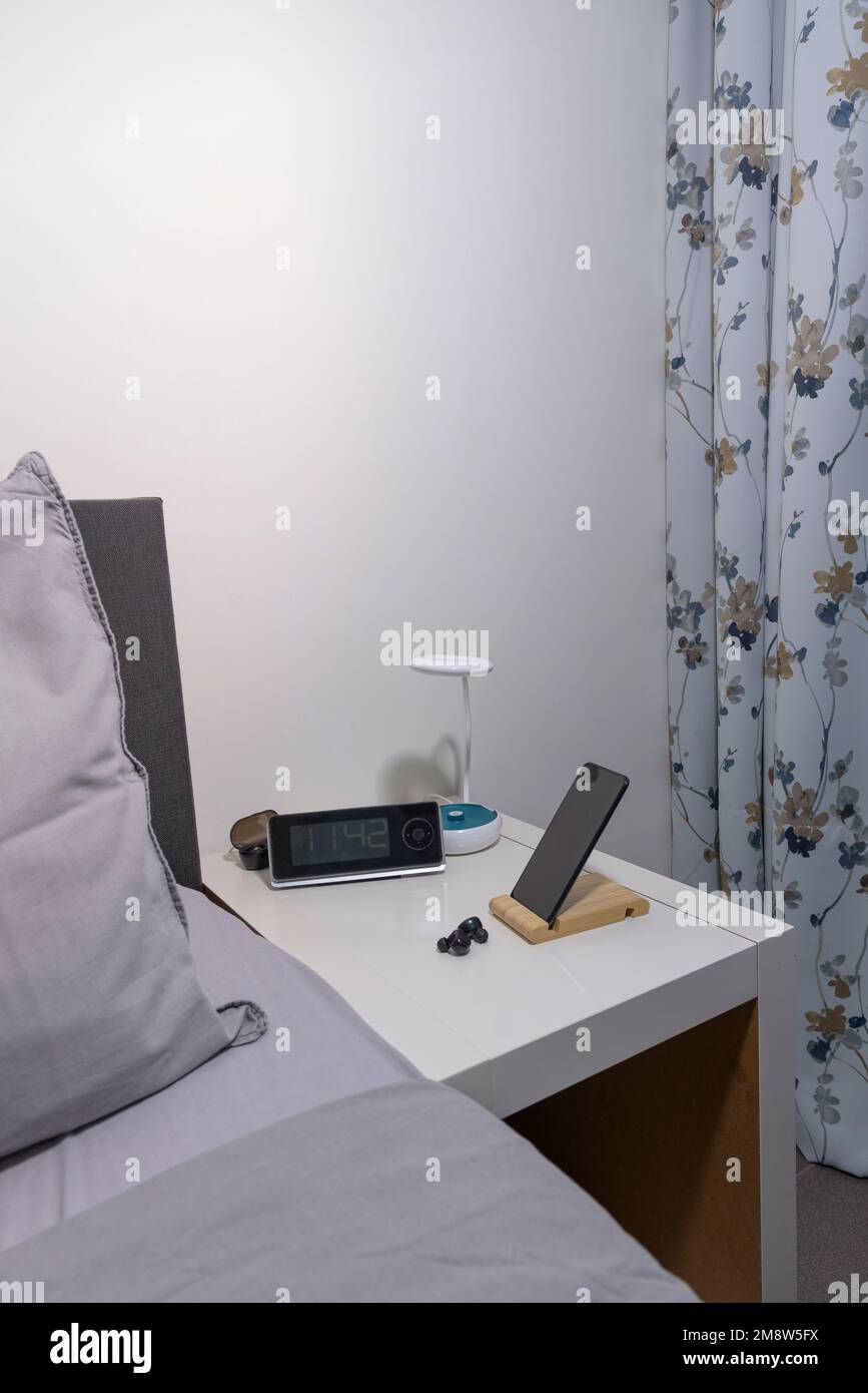 Smartphone sul comodino con lampada, cuffia, orologio e frammento di letto. Vista verticale Foto Stock