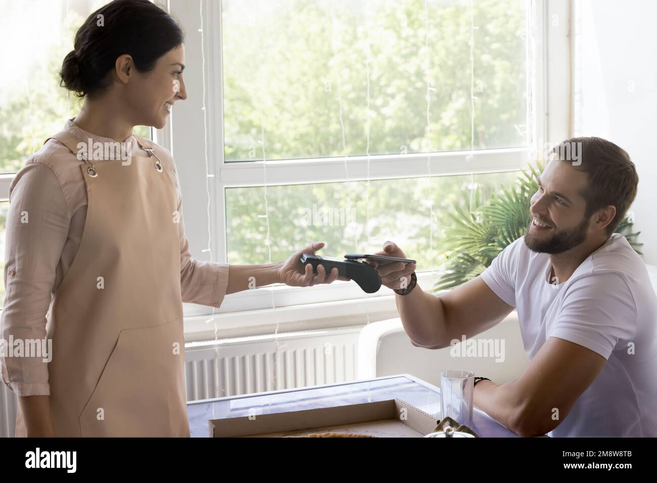 Cameriera e customer man che collegano telefono cellulare e terminale Foto Stock