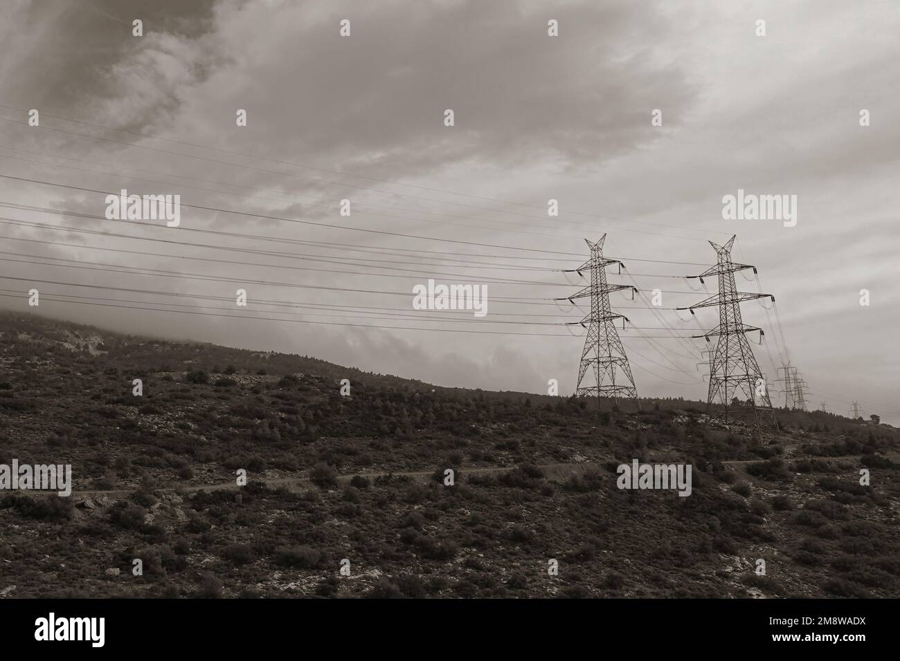 Piloni linee elettriche aeree su montagne nebbiose e cielo nuvoloso d'inverno. Tinta bianco e nero. Foto Stock