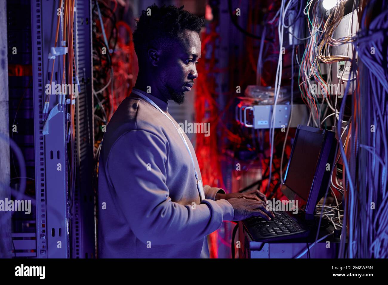 Vista laterale ritratto di uomo nero come amministratore di rete impostazione dei server e utilizzo di laptop in luce al neon Foto Stock