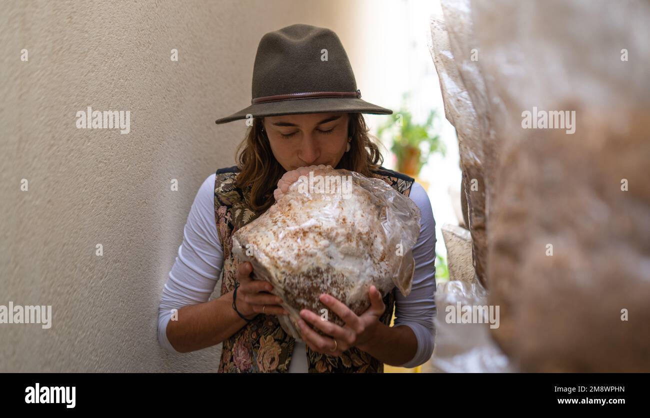 Giovane donna che tiene il substrato di micelio con i funghi della criniera del leone e sniffing esso Foto Stock
