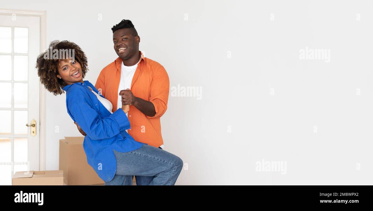 Felice giovane sposi neri che ballano insieme nella stanza luminosa mentre si sposta la casa Foto Stock