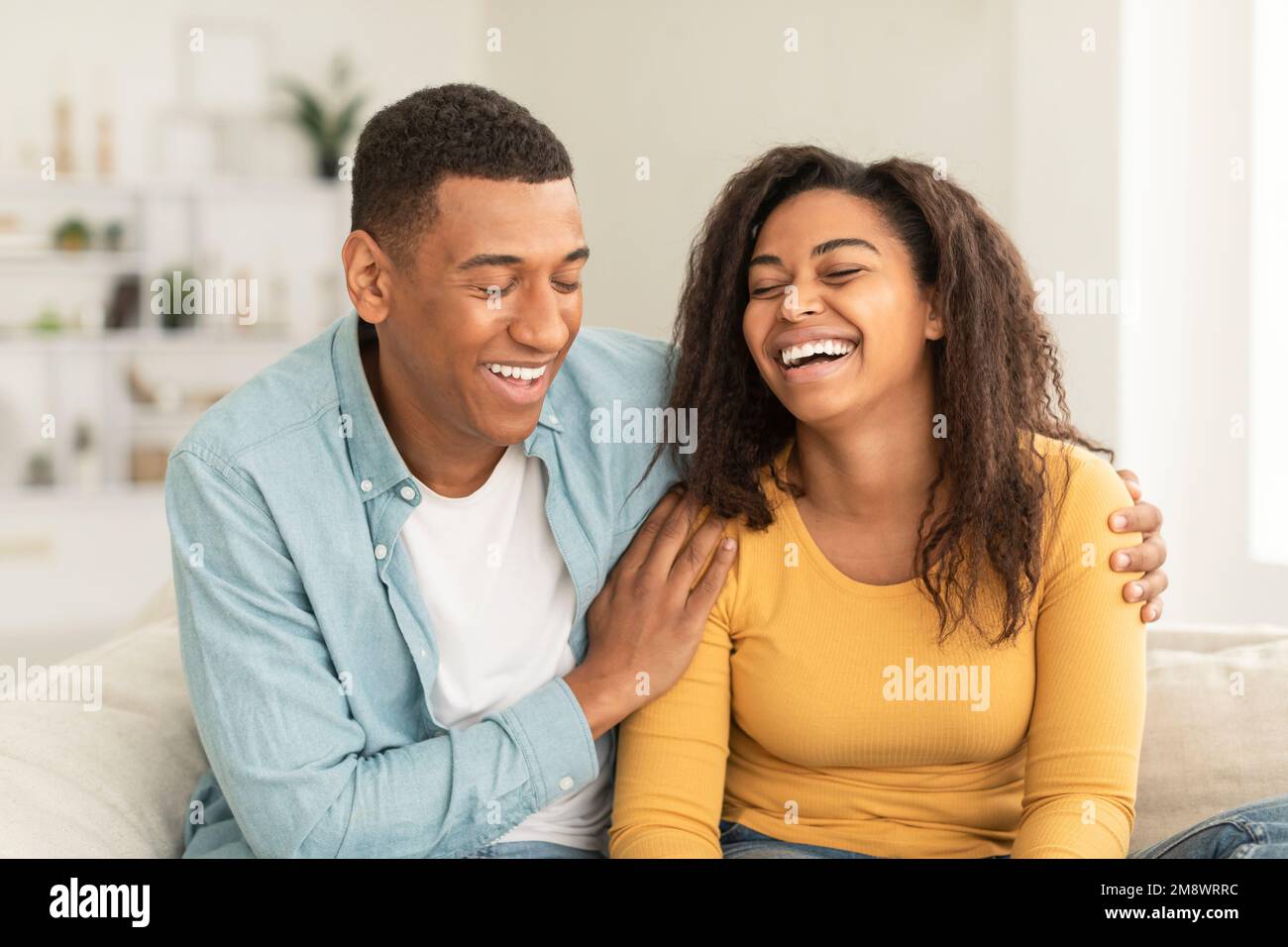 Ridendo bella giovane afroamericana e abbraccio ragazzo, divertirsi nel tempo libero, seduti sul divano Foto Stock