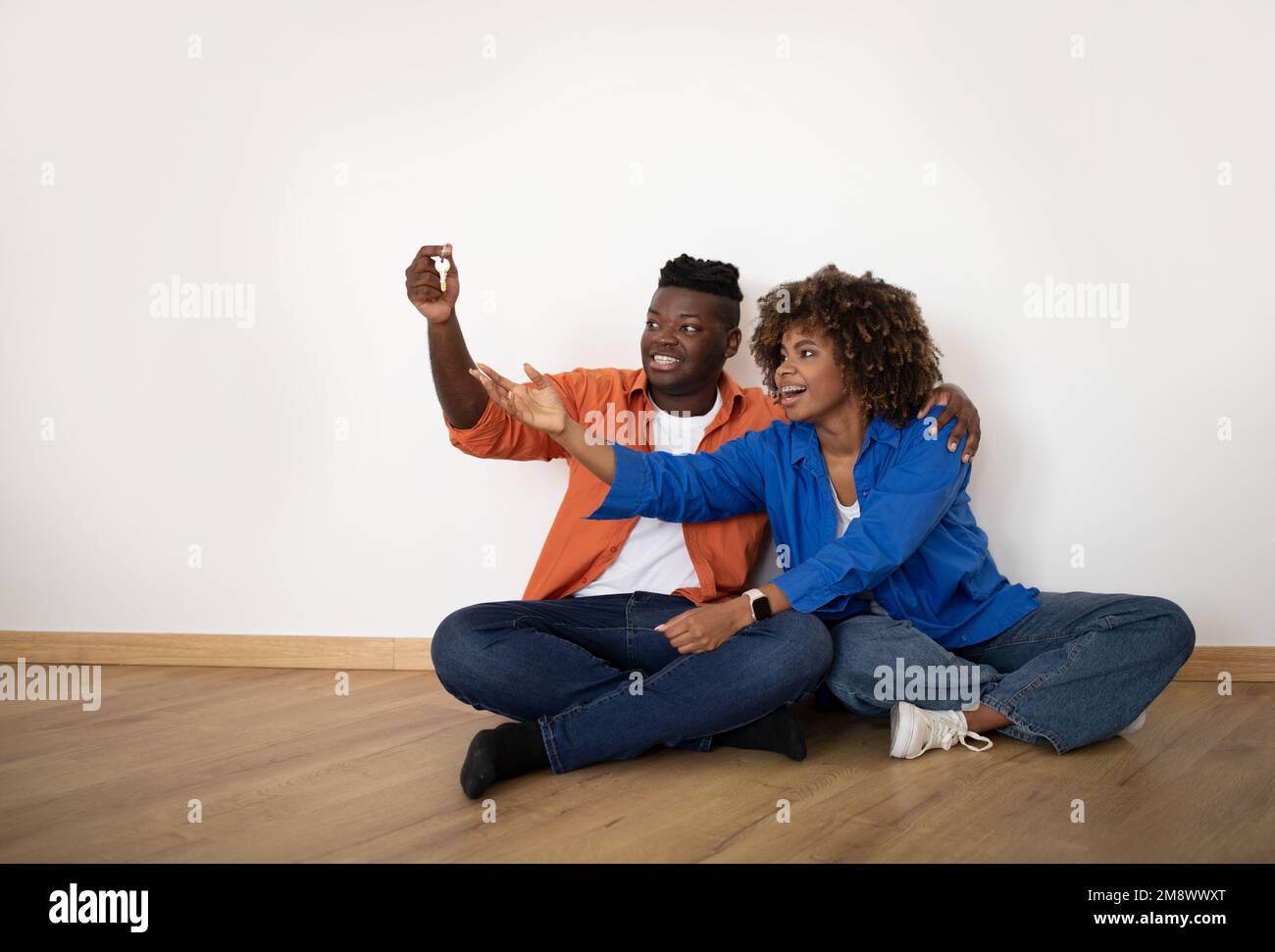 Sposi neri giovani felici che siedono sul pavimento e che tiene le chiavi domestiche Foto Stock