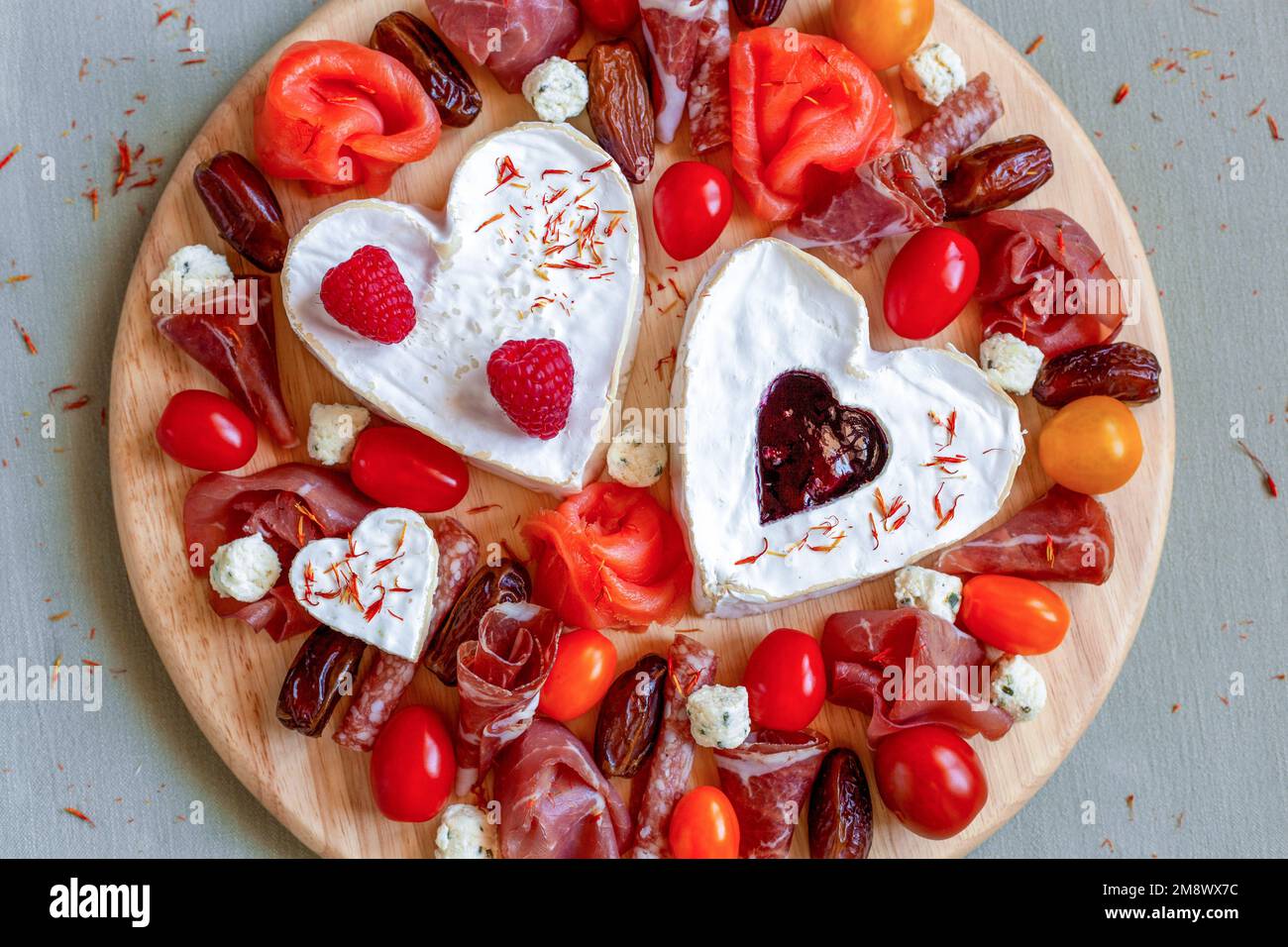 piatto di formaggi con formaggio a forma di cuore, frutta e delicatessen, decorato con fiori commestibili Foto Stock