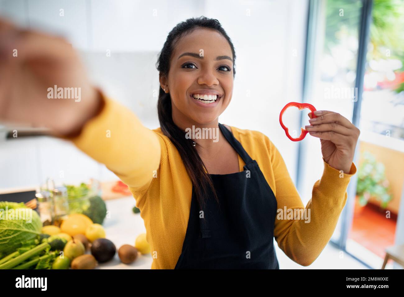 Sorridente giovane afro-americana femmina in grembiule con pezzettino di pepe fa selfie con verdure Foto Stock