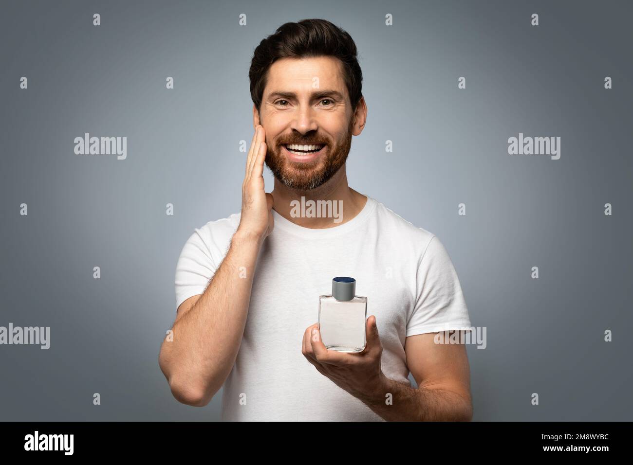 Governare e concetto di persone. Buon uomo caucasico che applica profumo sulla barba, sfondo grigio studio Foto Stock