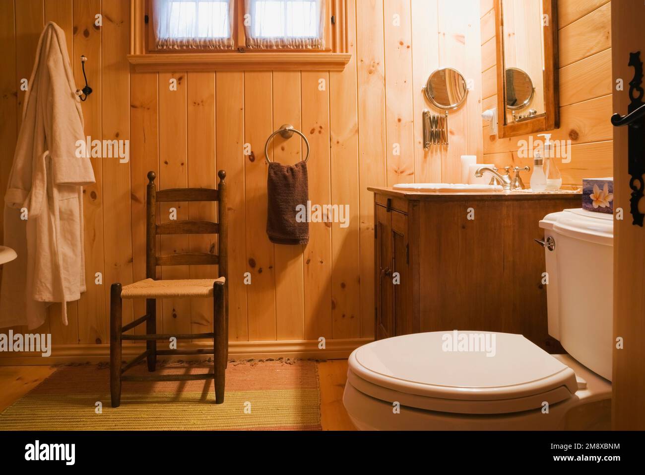 Antica sedia in legno con schienale alto, lavandino e WC nel bagno principale al piano superiore all'interno di una casa in legno macinato. Foto Stock