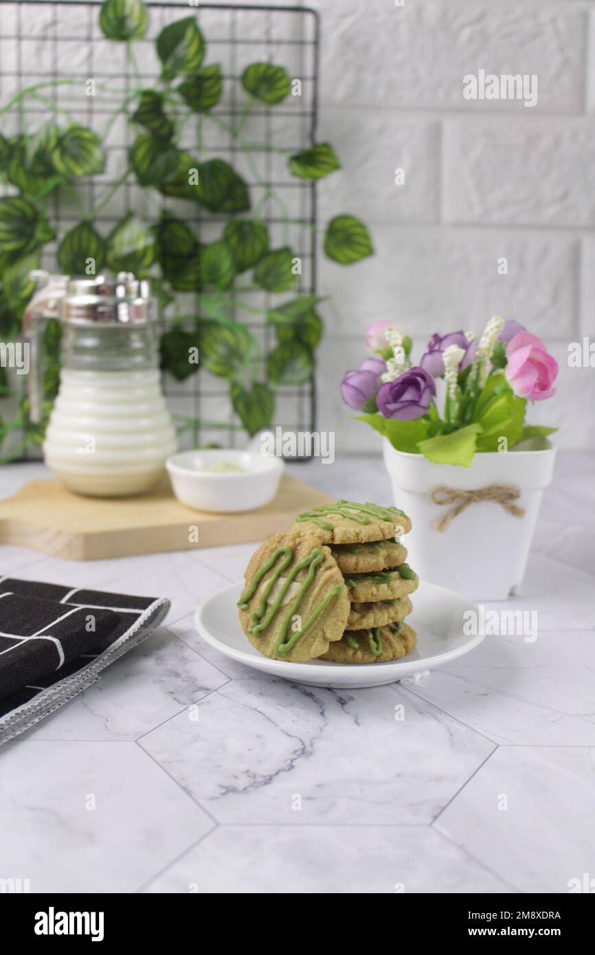 Biscotti al tè verde serviti su un piatto bianco con un bicchiere di latte sullo sfondo. Hanno un sapore leggermente dolce e una consistenza croccante. Foto Stock