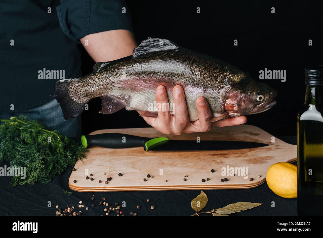 grande pesce fresco in cucina nelle mani dello chef sullo sfondo del tavolo con ingredienti per la cottura. Trota arcobaleno Foto Stock