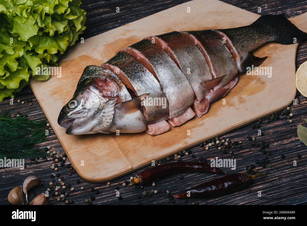 Trota tagliata a pezzi su un asse di legno. Pesce rosso fresco sul tavolo con ingredienti Foto Stock