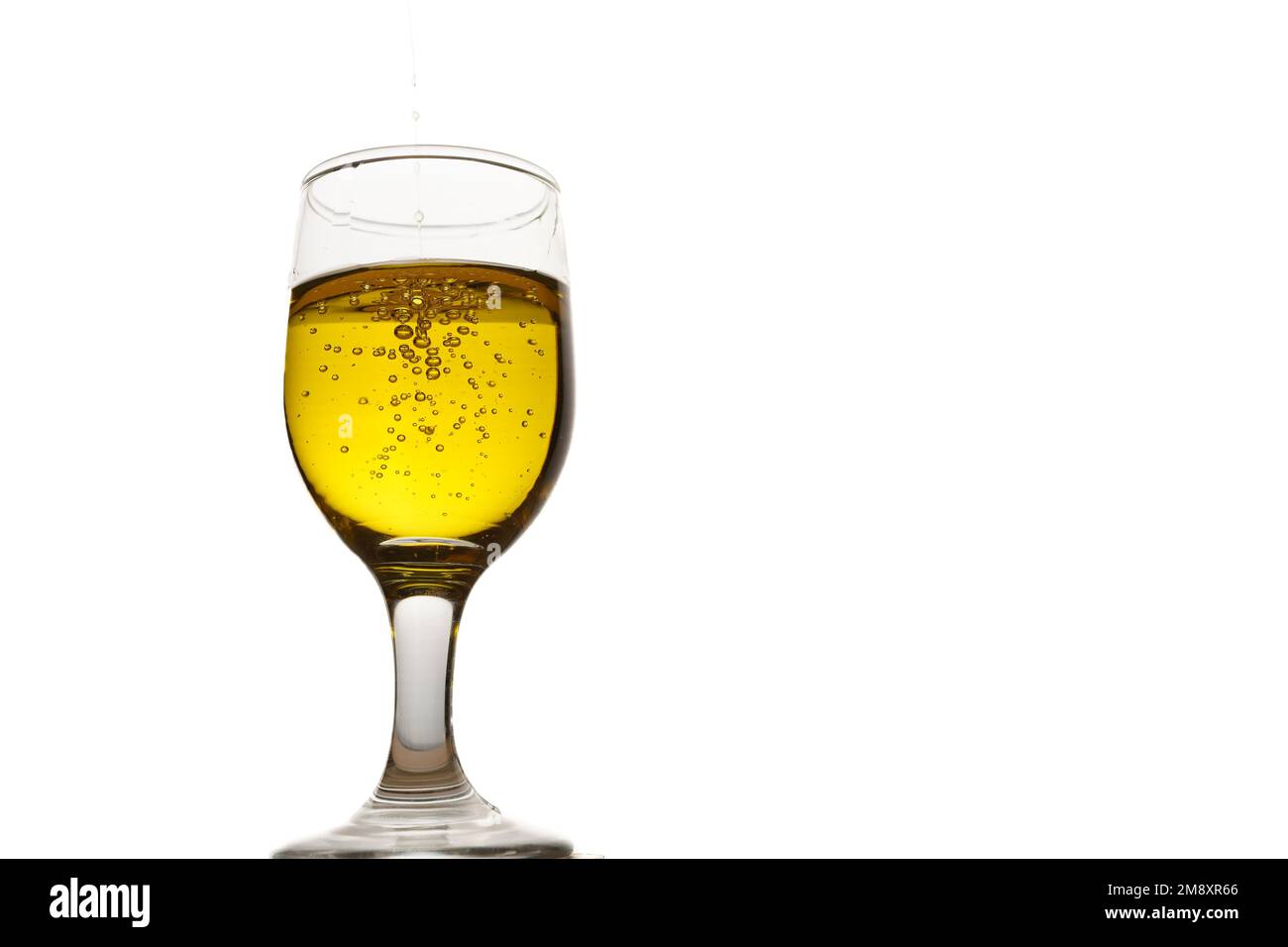 Primo piano di una tazza di vetro con olio extravergine di oliva con bollicine su fondo bianco Foto Stock