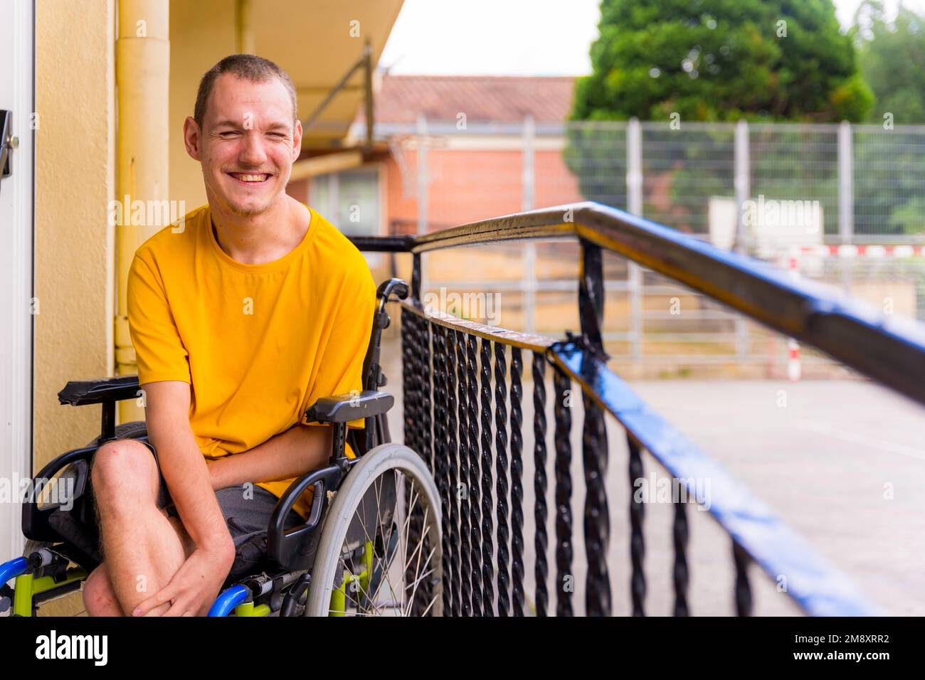 Disabile vestito di giallo in una sedia a rotelle a scuola sorridente Foto Stock