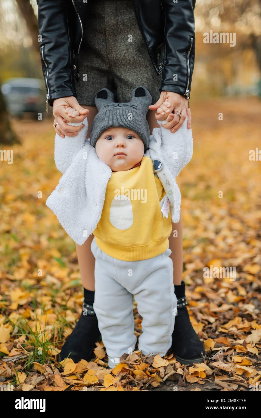 Il bambino impara a fare i primi passi tenendo le mani della mamma in autunno nel Parco Foto Stock