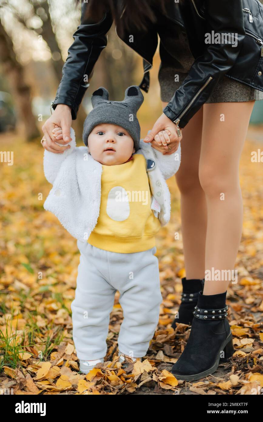 Il bambino impara a fare i primi passi tenendo le mani della mamma in autunno nel Parco Foto Stock