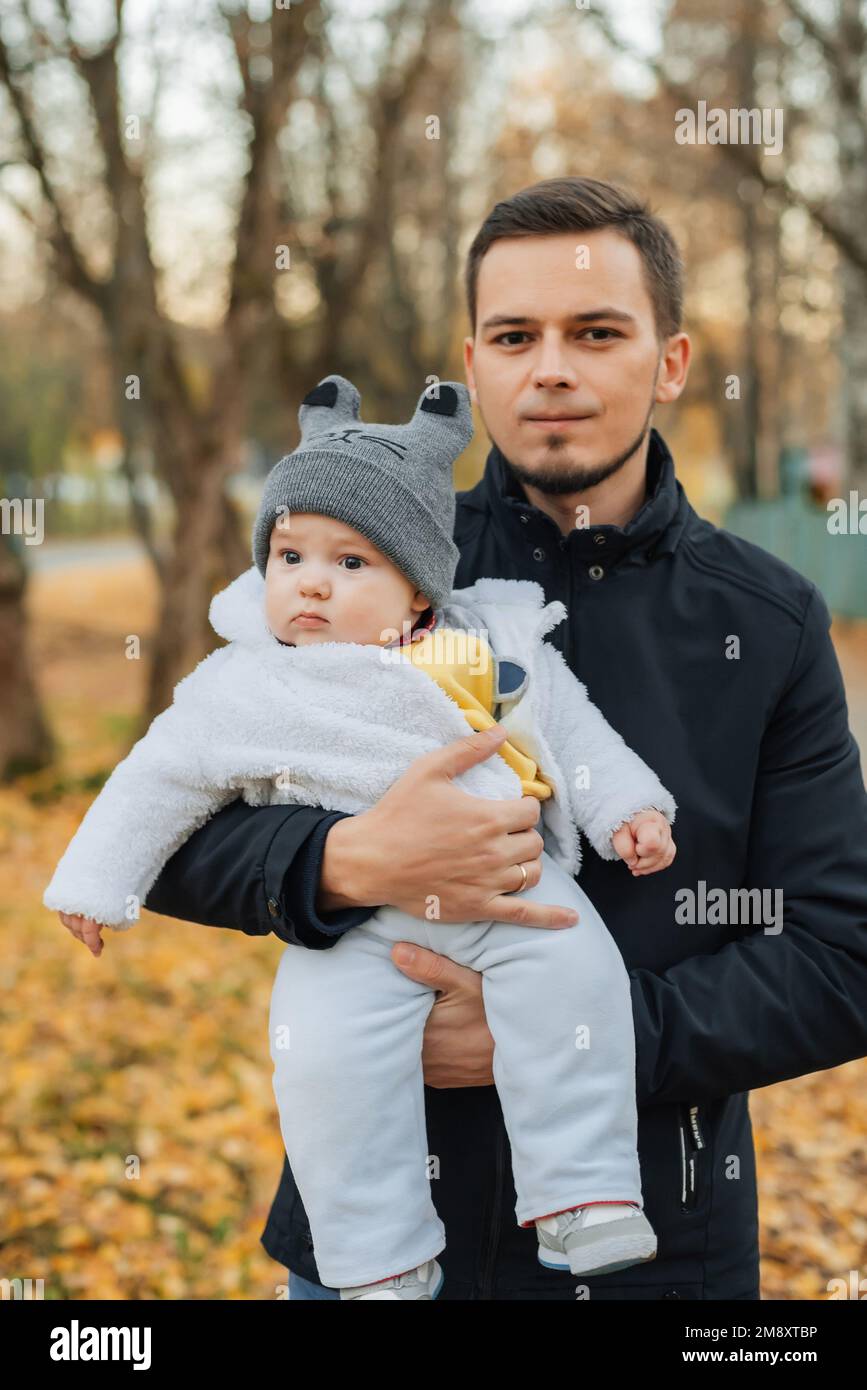 Il giovane papà caucasico tiene nelle sue mani il bambino piccolo figlio in autunno nel Parco Foto Stock