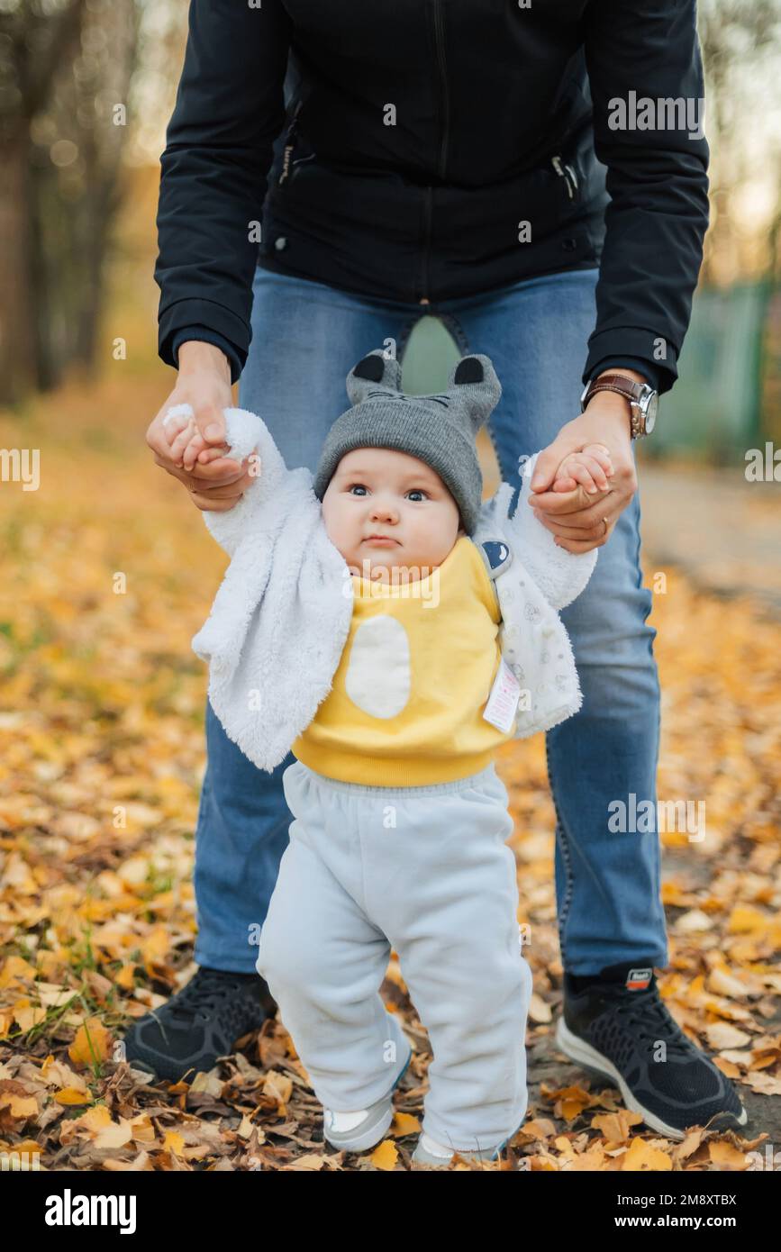 Il bambino impara a fare i primi passi tenendo le mani del papà in autunno nel Parco Foto Stock
