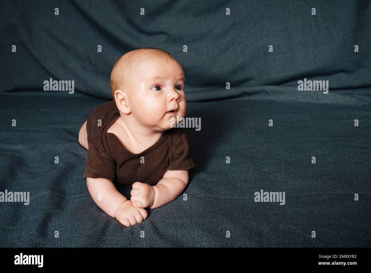 Neonato sdraiato su una coperta. Piccolo bambino caucasico in un bodysuit marrone. Foto Stock