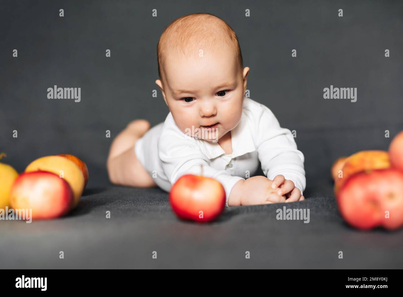 Neonato sdraiato con le mele. Bambino caucasico in un bodysuit bianco. Concetto di infanzia autunnale Foto Stock