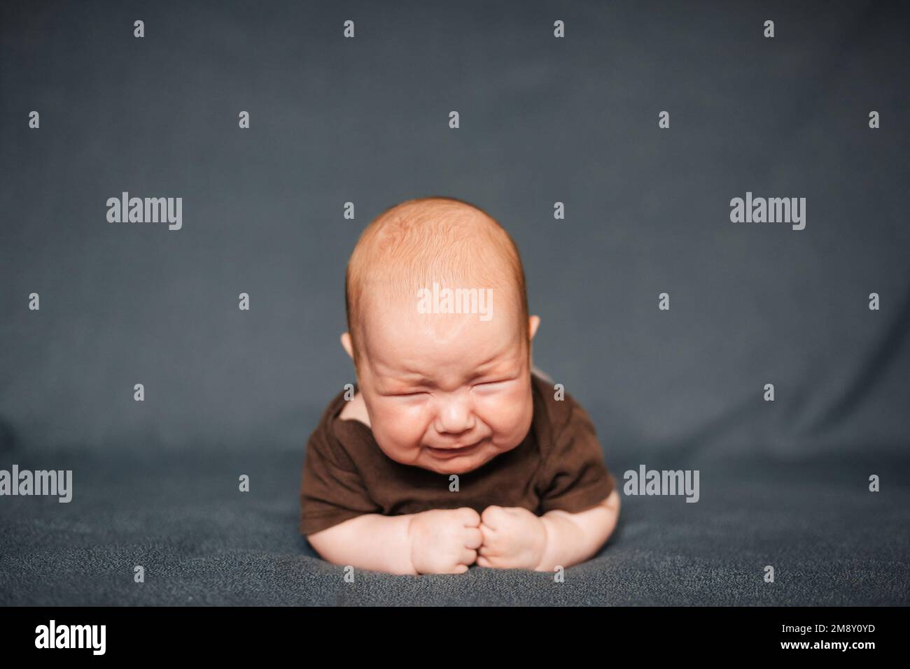 Bambino neonato che piange. Il bambino caucasico è sdraiato su una coperta grigia Foto Stock