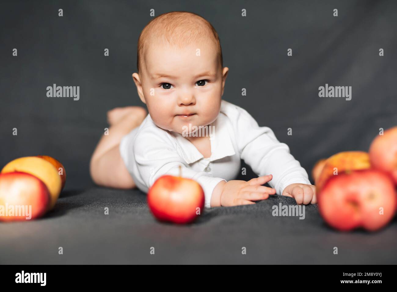 Neonato sdraiato con le mele. Bambino caucasico in un bodysuit bianco. Concetto di infanzia autunnale Foto Stock