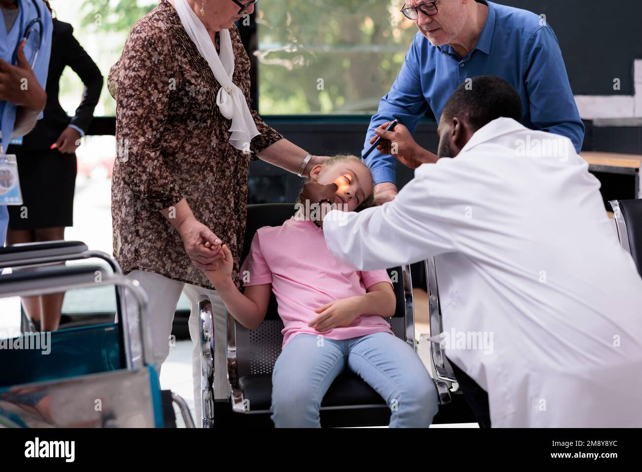 Medico medico che illumina l'occhio di un bambino mentre esamina i riflessi della pupilla durante la visita di controllo nella zona di attesa dell'ospedale. Bambino inconscio svenente sulla sedia Foto Stock