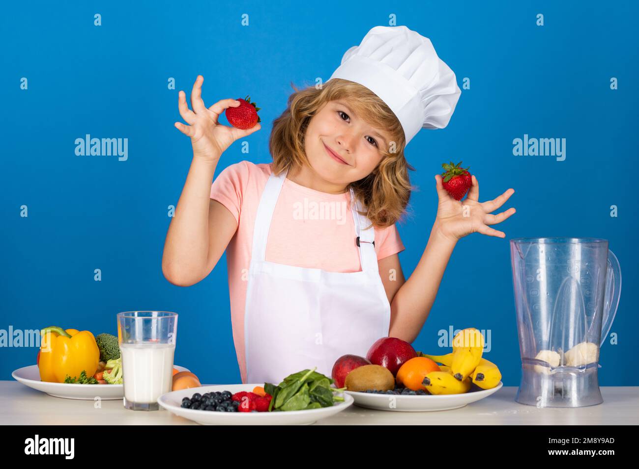 Bambino che indossa uniforme cuoco e cappello cuoco preparare verdure in  cucina tenere fragole, studio ritratto. Cucina, cucina e cibo per bambini  Foto stock - Alamy