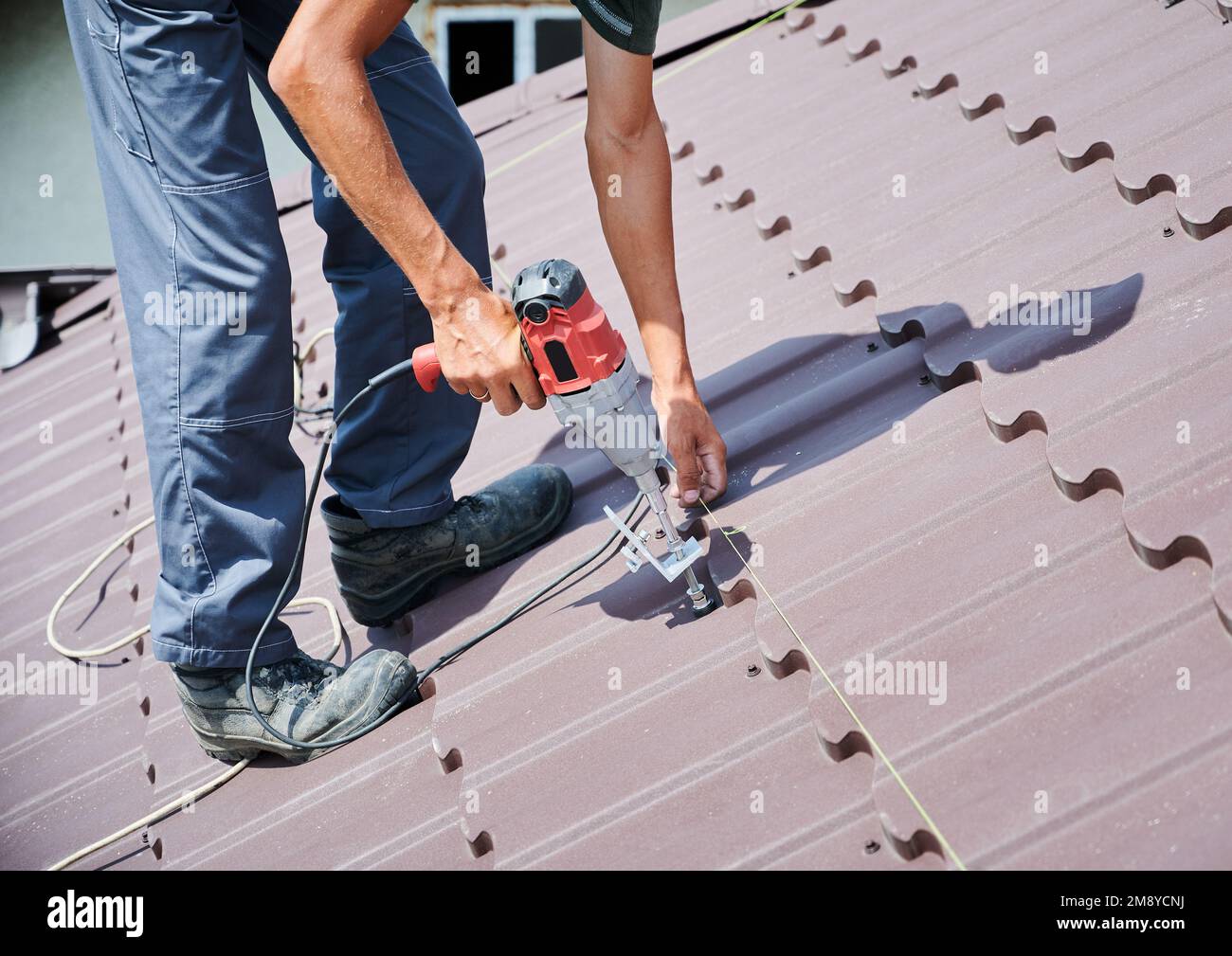 Lavoratore prepearing per l'installazione di pannelli solari fotovoltaici sul tetto della casa. Primo piano man installer che lavora con il cacciavite elettrico. Foto Stock