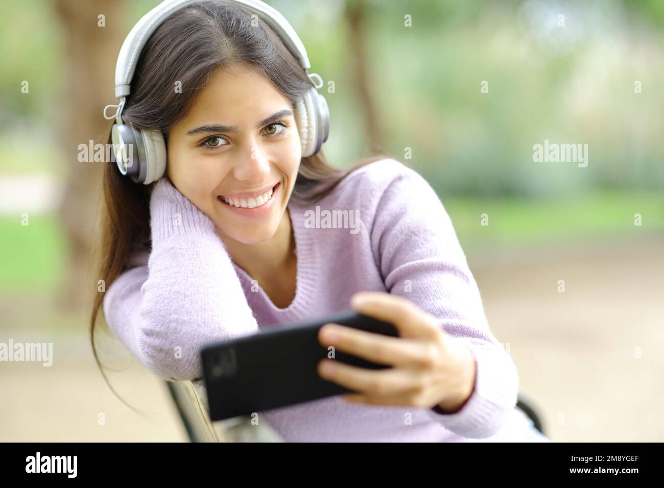Donna felice che ascolta la musica che ti guarda in un parco Foto Stock