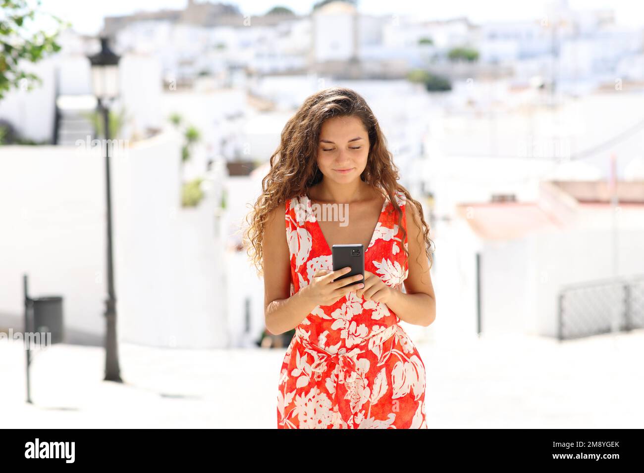 Vista frontale ritratto di un turista a piedi e utilizzando smartphone in una città bianca in vacanza Foto Stock