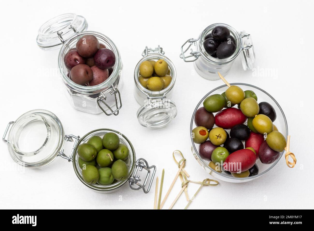 Olive in vasetti di vetro. Spiedini sul tavolo. Giacitura piatta. Sfondo bianco. Foto Stock