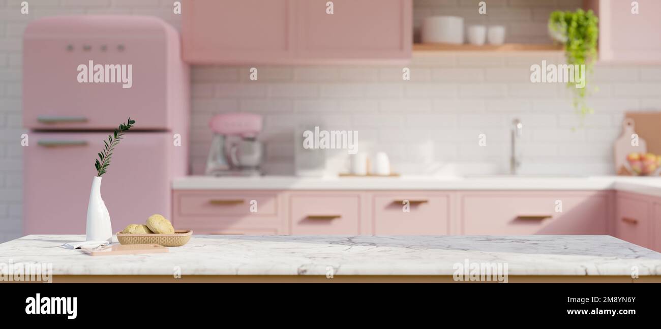 Spazio copia per l'esposizione dei prodotti su un tavolo in marmo bianco con decorazioni in una splendida cucina rosa pastello con armadio da cucina rosa, frigorifero rosa e angolo cottura Foto Stock