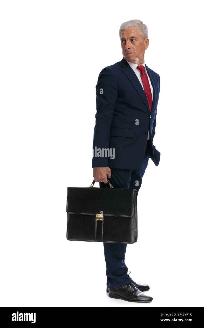 Immagine completa del corpo e vista laterale di un vecchio uomo d'affari che guarda indietro sulla spalla e tiene una valigetta Foto Stock