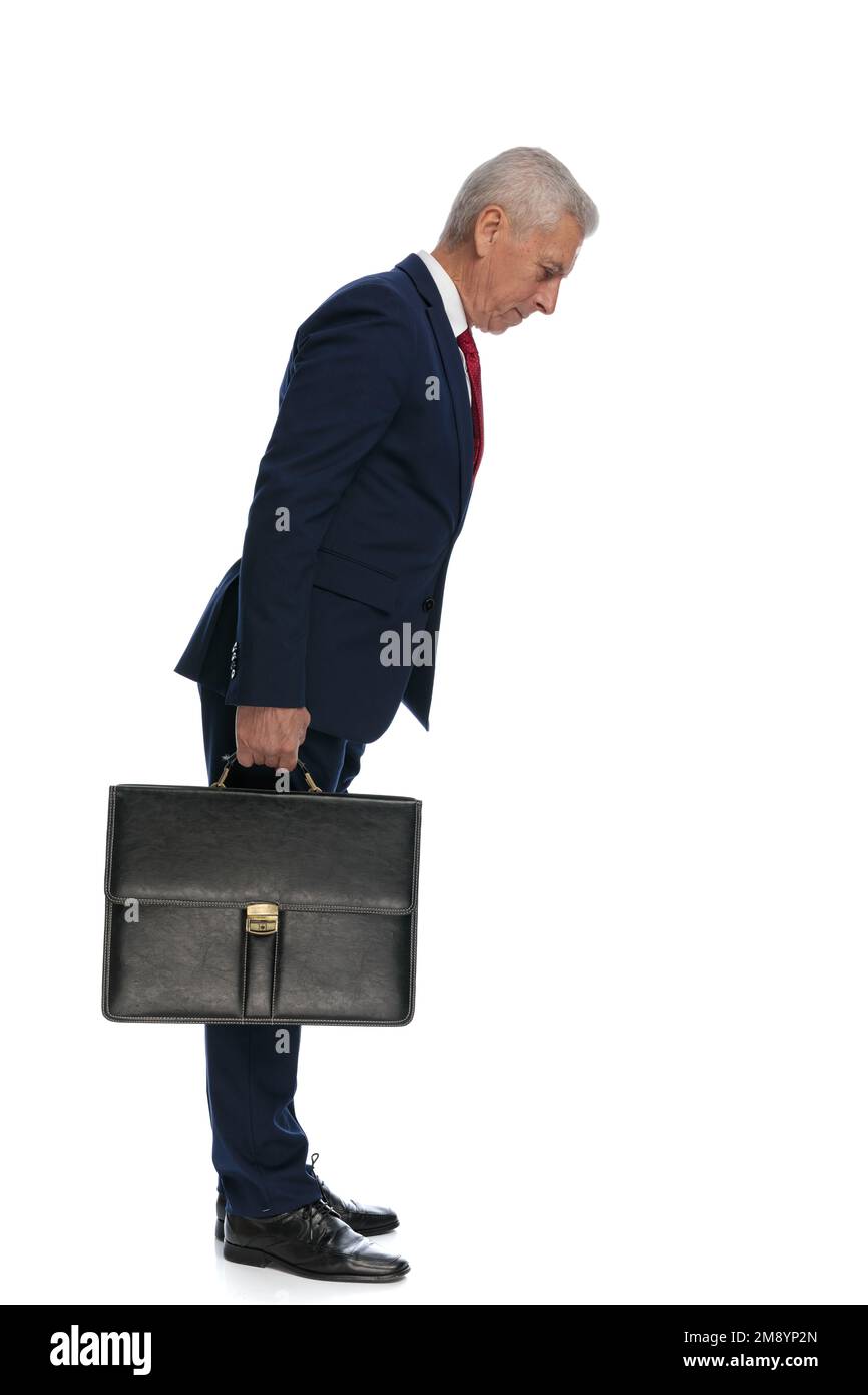 Immagine completa del corpo e vista laterale di un vecchio uomo d'affari che si inclina in avanti per controllare qualcosa mentre tiene una valigetta Foto Stock