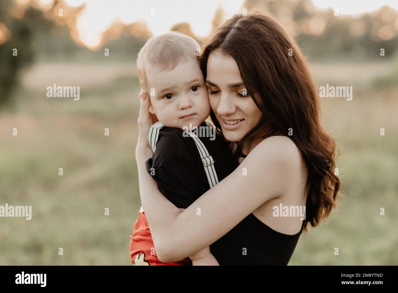 La giovane madre caucasica sorride abbracciando il figlio in estate in un campo in natura. La grana aggiunta simula la pellicola Foto Stock