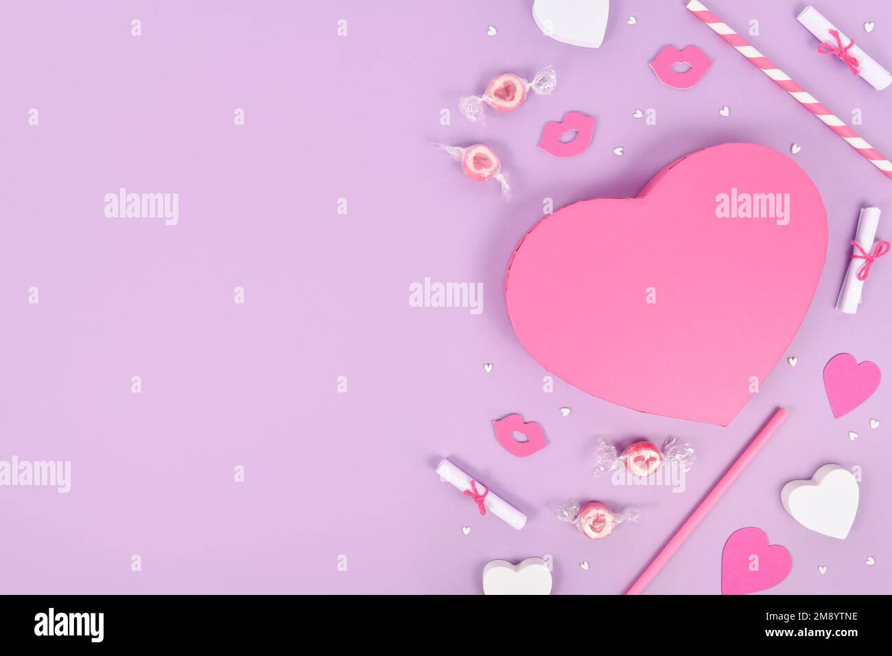Piatto di San Valentino color pastello con scatola regalo a forma di cuore, ornamenti a cuore e caramelle su sfondo viola con spazio copia Foto Stock