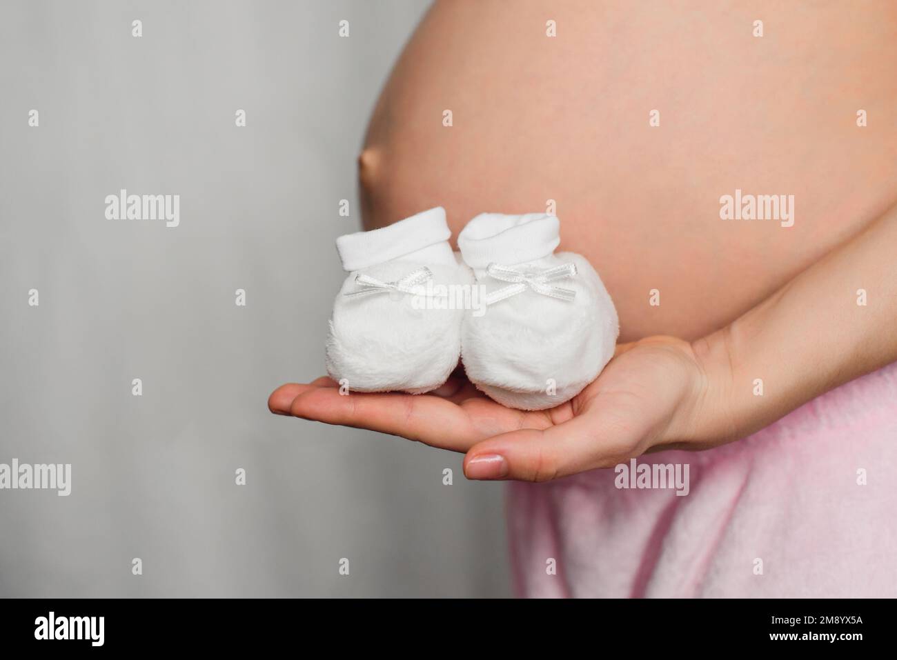 stivaletti per neonati nelle mani di una bambina incinta sullo sfondo dell'addome in attesa del bambino Foto Stock