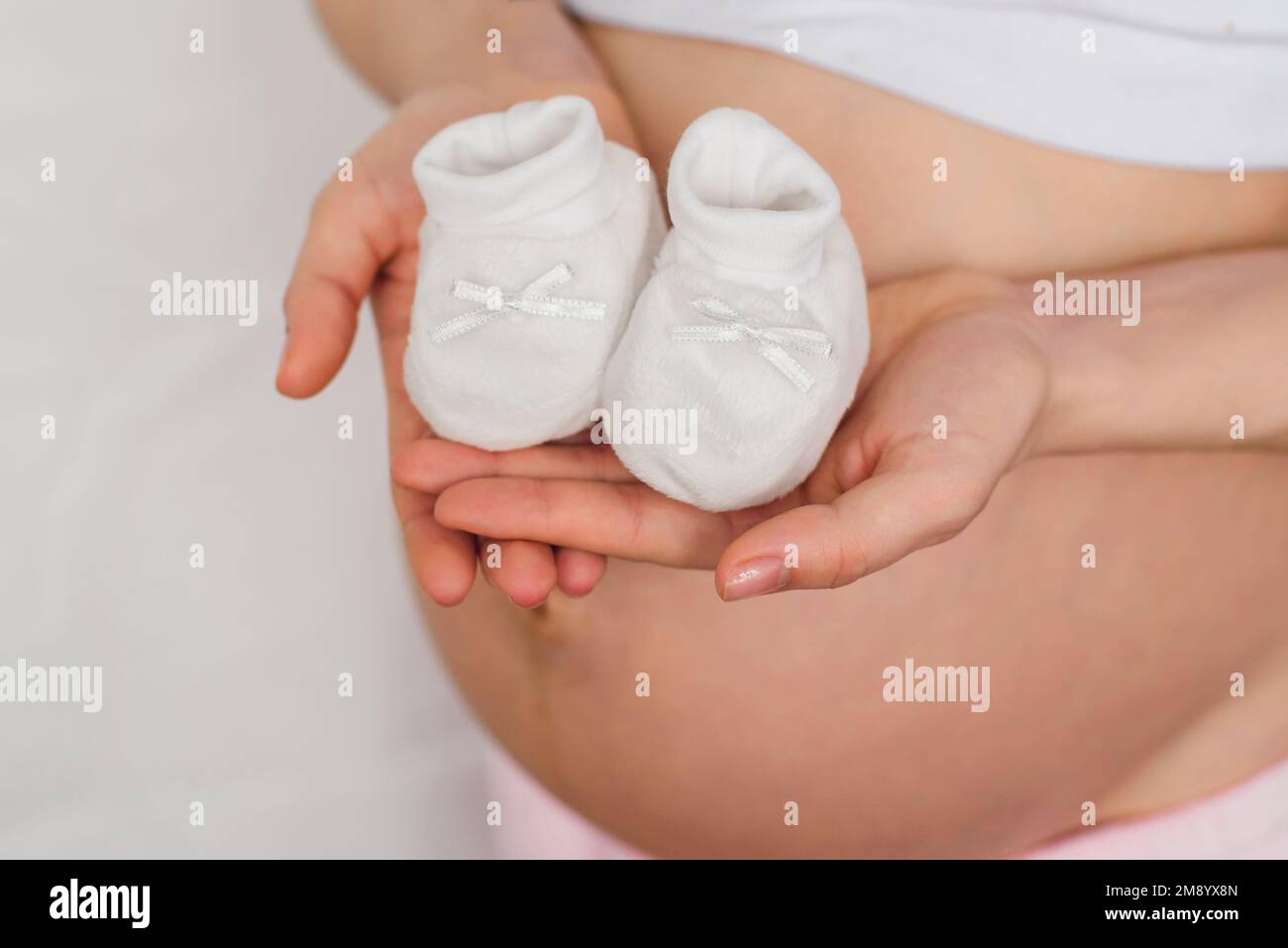 stivaletti per neonati nelle mani di una bambina incinta sullo sfondo dell'addome in attesa del bambino Foto Stock