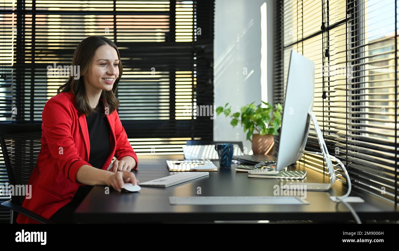Sorridente imprenditore caucasico guardando lo schermo del computer che lavora online presso un ufficio contemporaneo Foto Stock