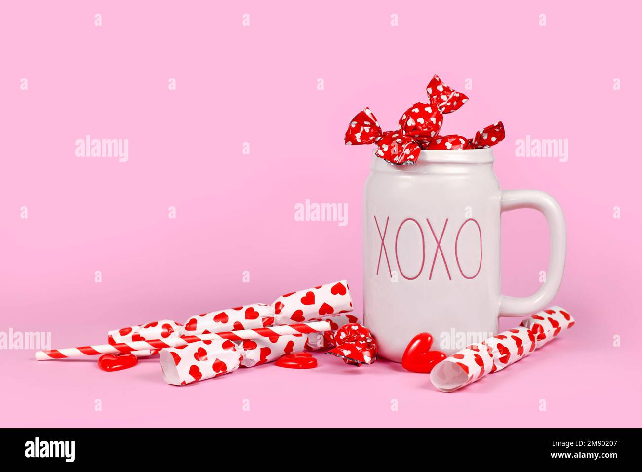 Addobbo grazioso di San Valentino con cuori, caramelle rosse e tazza XOXO su sfondo rosa Foto Stock