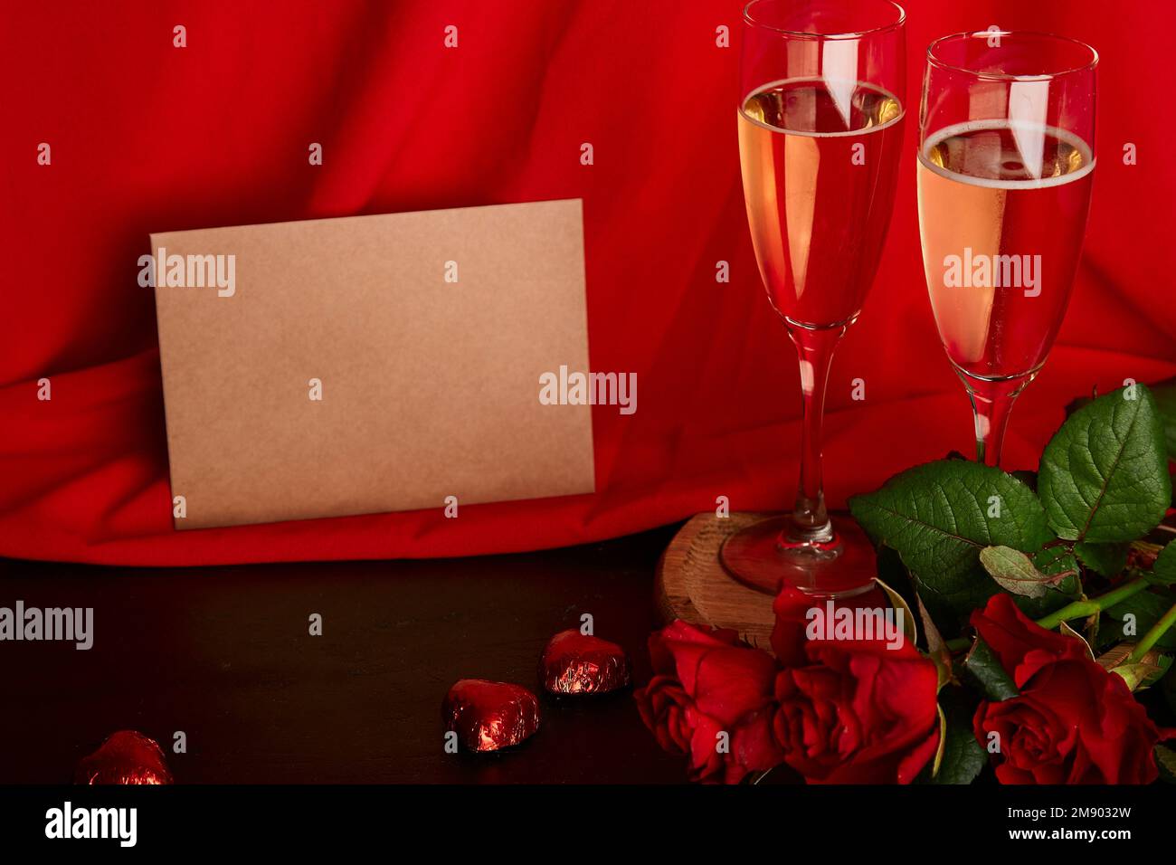 Estetica San Valentino cartolina mockup. Cena romantica di stagione rossa con cartolina, bicchieri di champagne, rose rosse e caramelle al cioccolato. Foto Stock