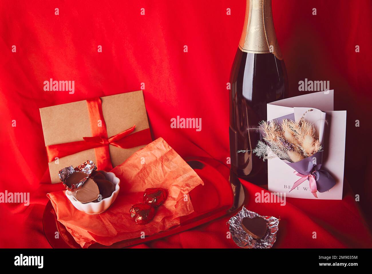 Cartolina giorno di San Valentino estetica. Cena romantica di stagione rossa con omaggio, cartolina, champagne e caramelle al cioccolato. Foto Stock