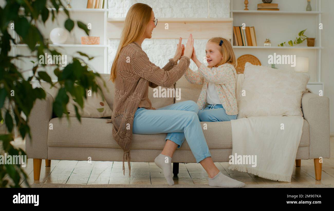 Allegro madre caucasica mamma femmina babysitter e cute felice bambino ragazza bambino bambino figlia giocare patty torta applaudire le mani a casa seduta sul divano Foto Stock