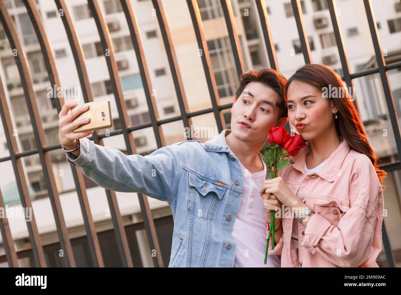 giovane coppia felice amore e romantico selfie al primo rapporto di data. ragazza asiatica sorpresa e sorridente al ragazzo dà fiori di rosa rossa a Foto Stock