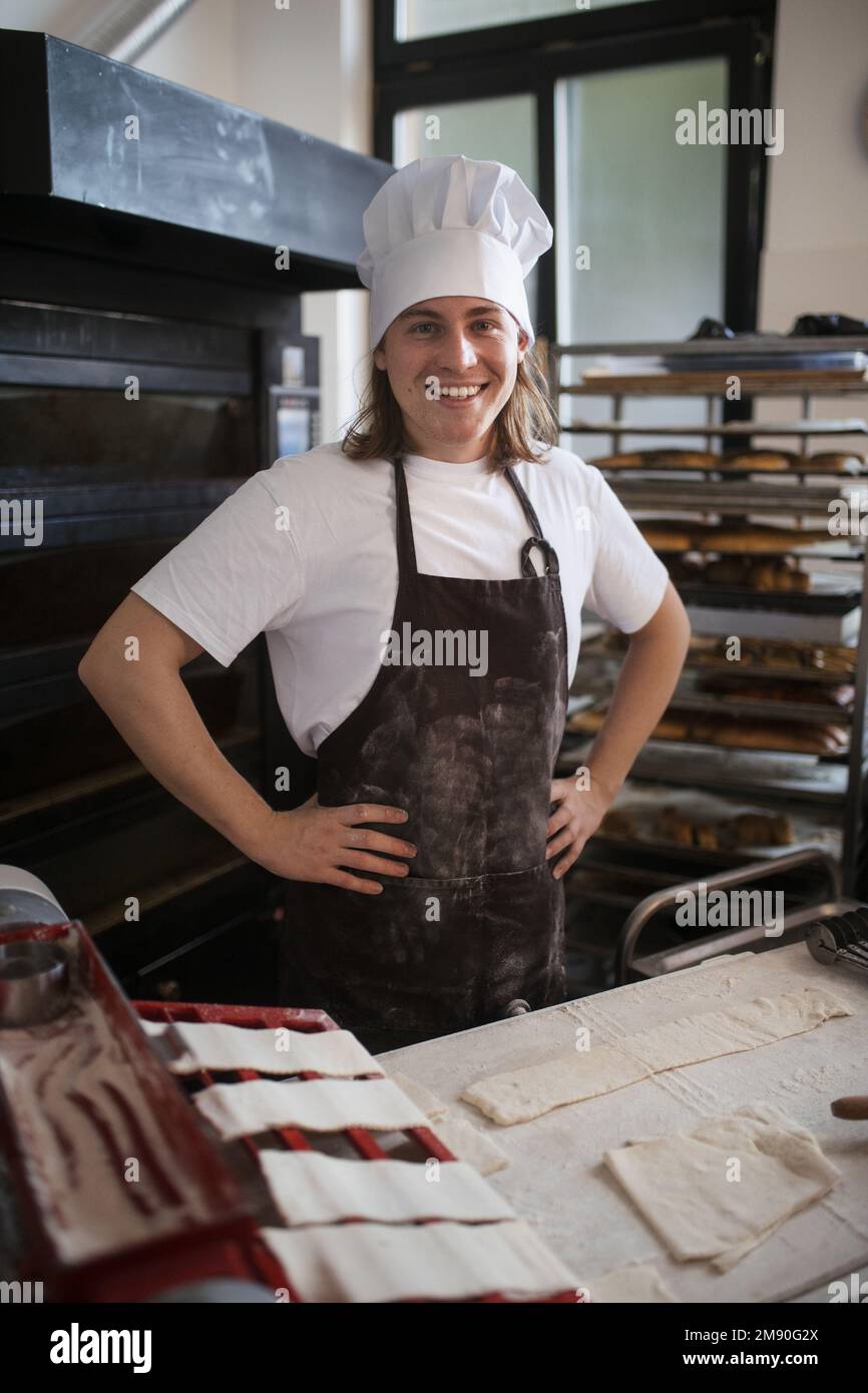 Panettiere giovane con cappellino dello chef che prepara dolci in panetteria. Foto Stock