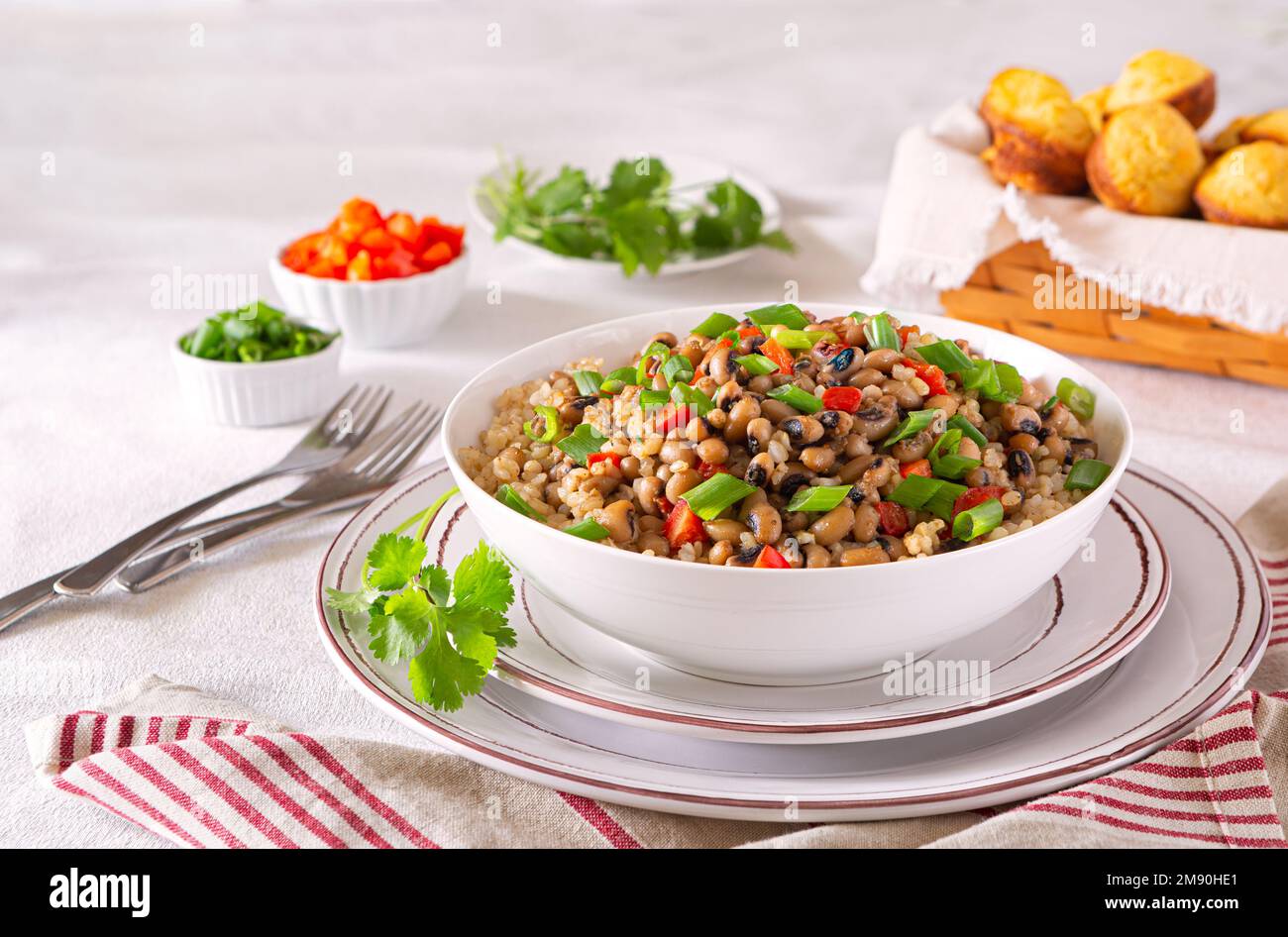 Versione a base di piante del piatto meridionale americano Hoppin John fatto con piselli dell'occhio nero, riso marrone, cipolla verde, peperone rosso e muffin al pane di mais Foto Stock