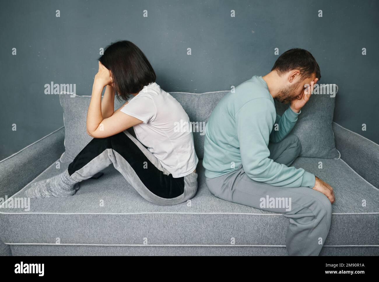 Una giovane coppia che si siede sul divano e guarda offesa mentre si è in disputa. Problemi di relazioni, disaccordo, conflitti nel matrimonio Foto Stock