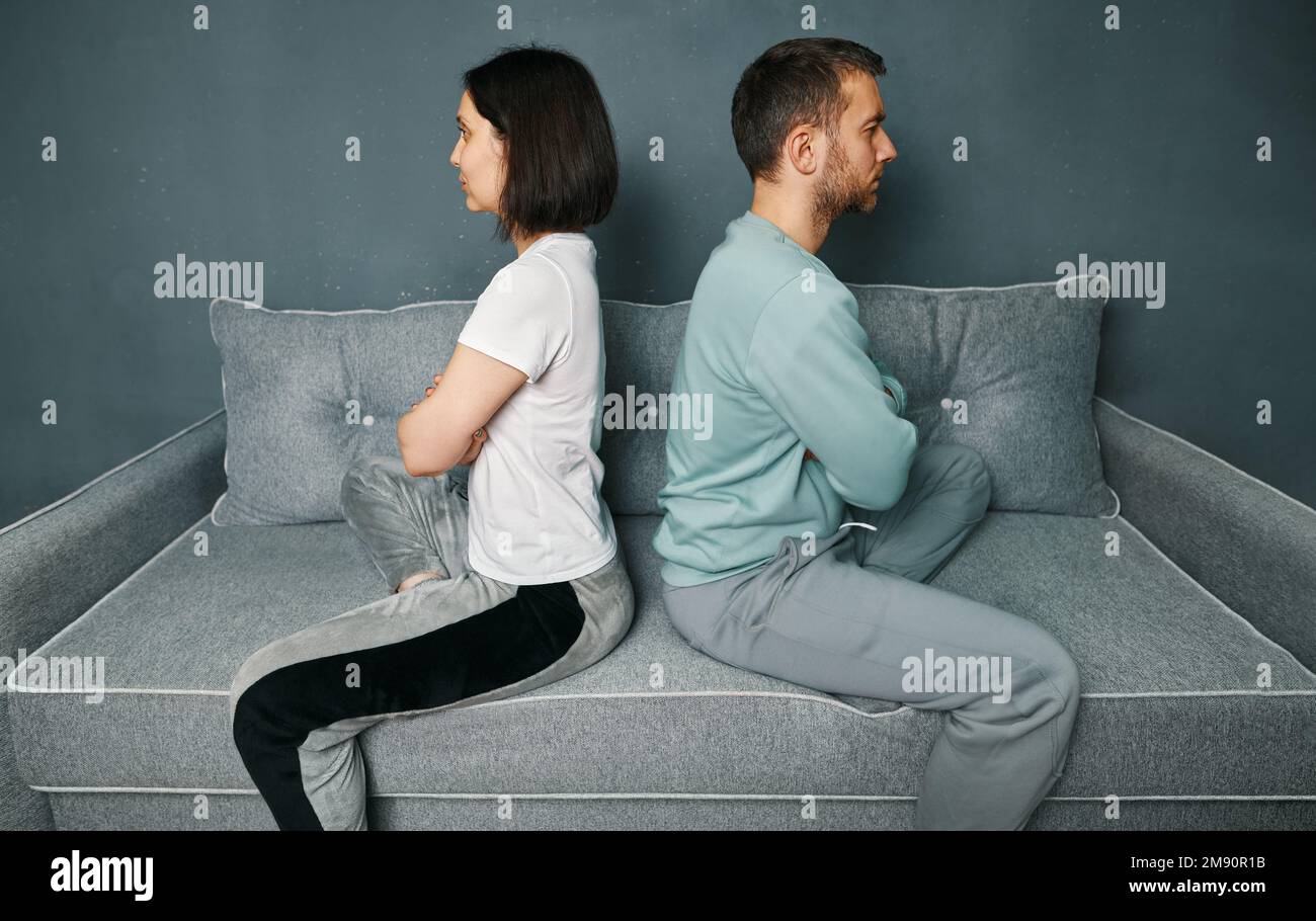 Una giovane coppia che si siede sul divano e guarda offesa mentre si è in disputa. Problemi di relazioni, disaccordo, conflitti nel matrimonio Foto Stock