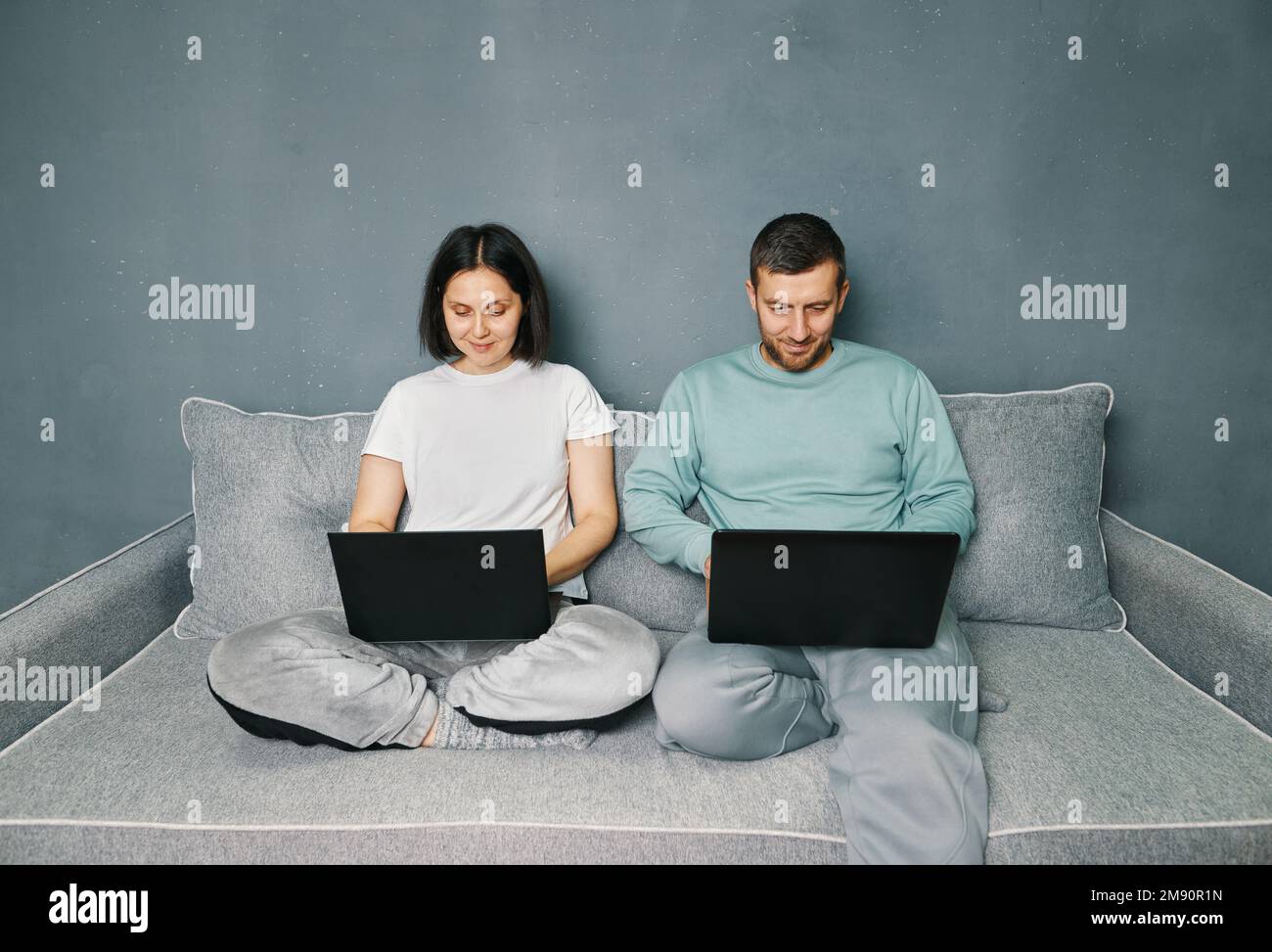 Giovane coppia che lavora sul computer portatile seduto sul divano a casa. Concetto di freelance. Foto Stock