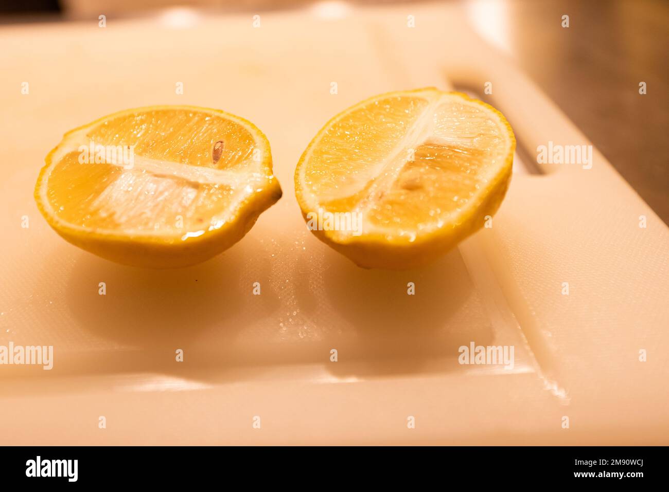 Un primo piano di un limone succoso tagliato a metà, su un tagliere in cucina, il concetto di preparazione del pasto Foto Stock